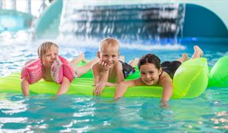 3 children lying on an air mattress in the pool of the bathing park