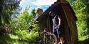 cyclist with bicycle in front of a small cabin