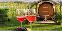 2 wine glasses stand on a table and wine barrel in the background