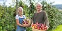 Elderly couple standing in front of fruit trees with fruit basket in hands